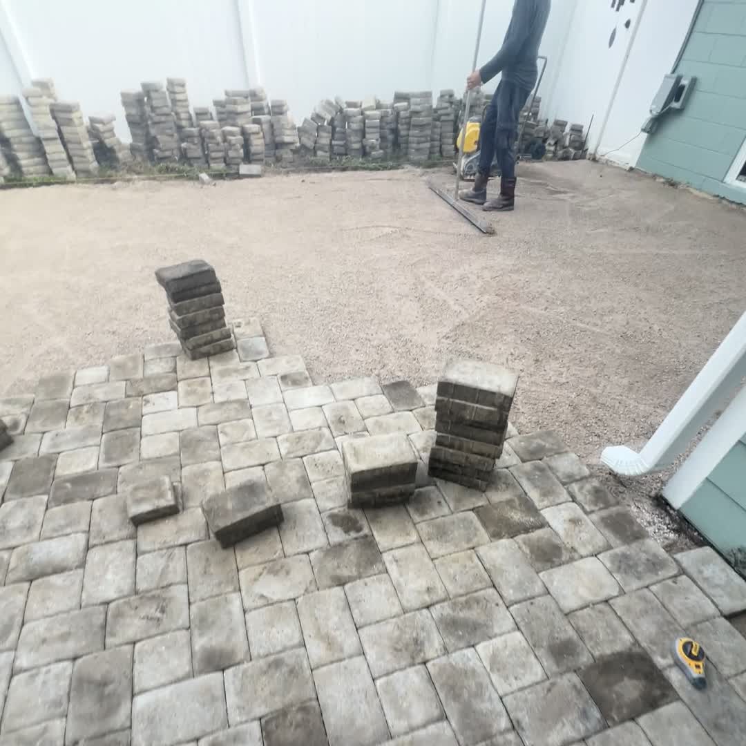 During: pavers stacked against the fence, plate compactor on the base