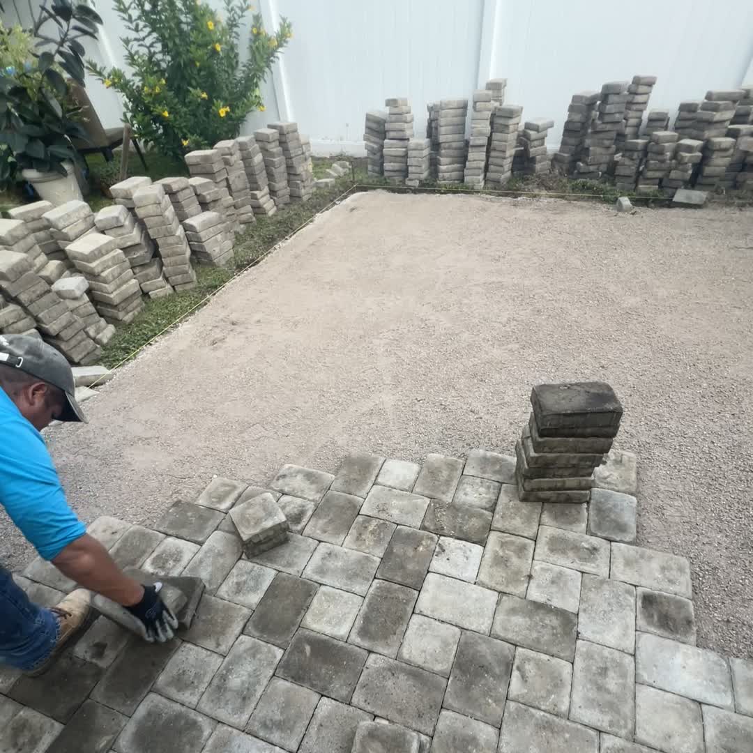 Fresh bedding sand screeded flat across a lifted patio section, the pavers stacked against the fence and the relay started from the house