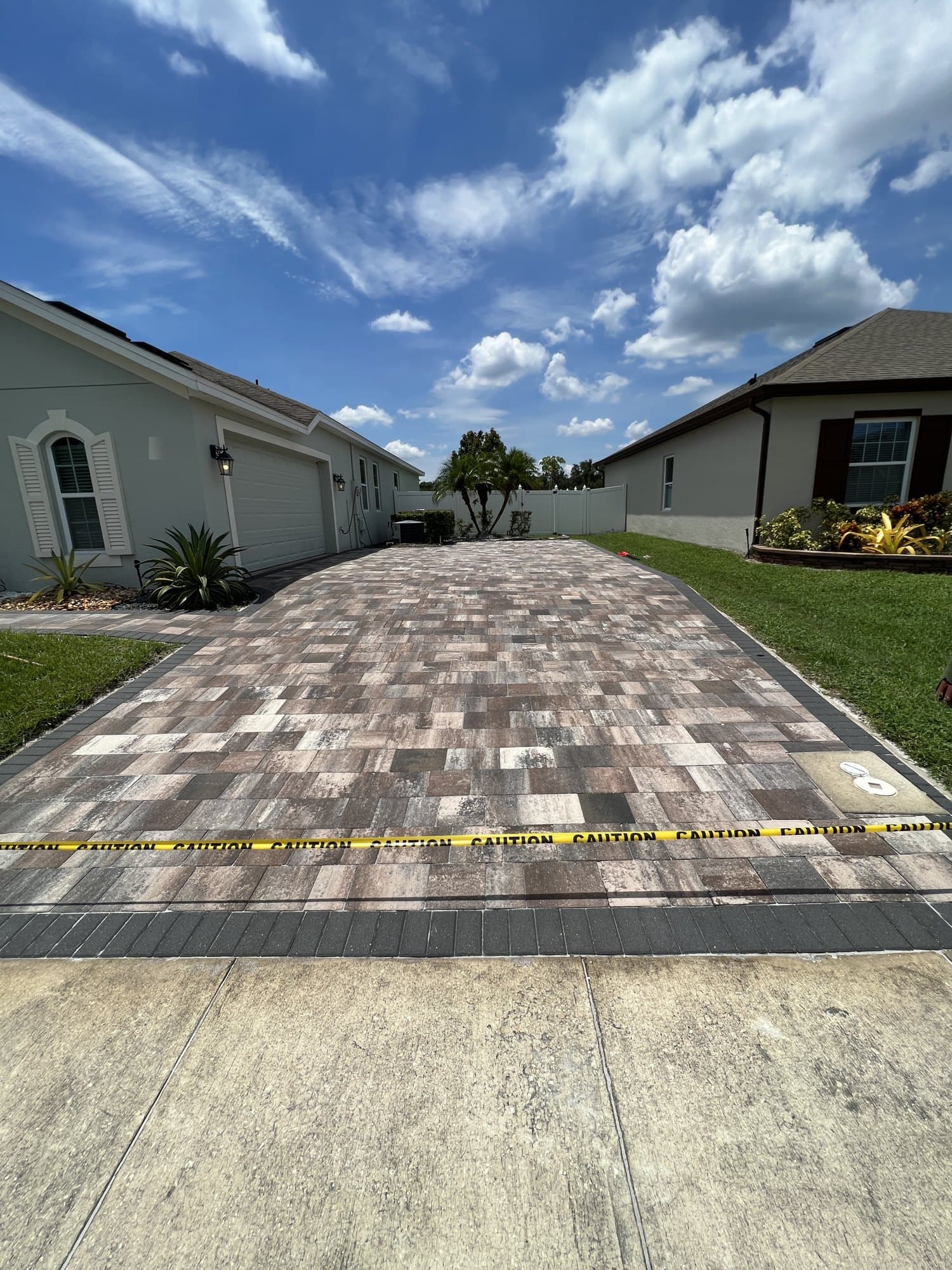 Sealed multi-tone paver driveway with a charcoal border, caution tape across the entrance