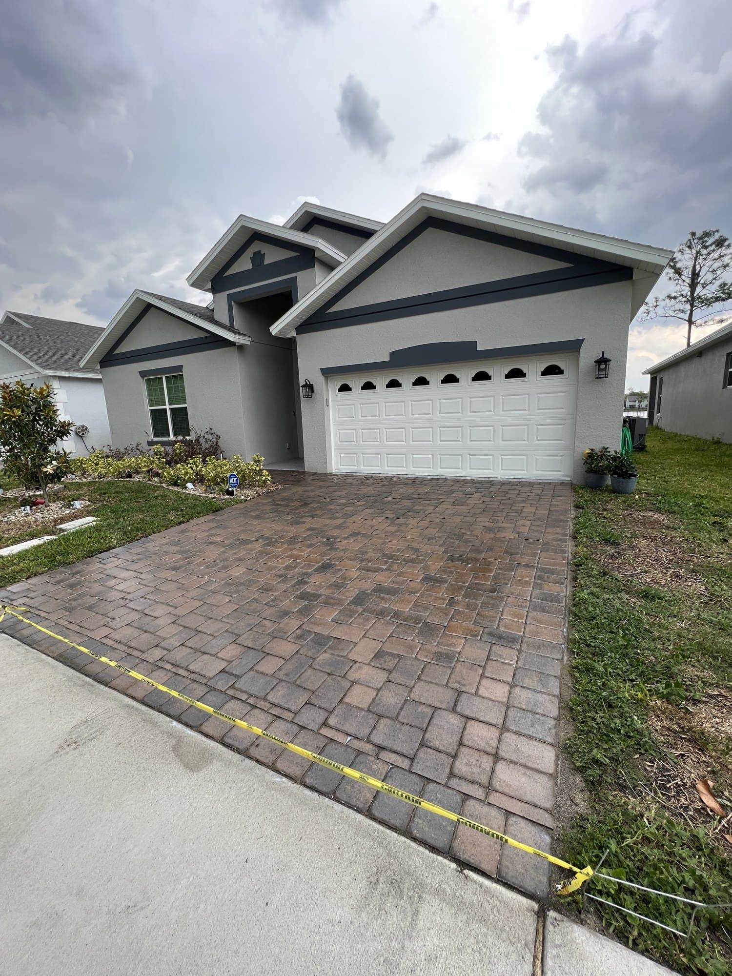 Freshly sealed paver driveway in front of a grey house, caution tape across the entrance while it cures
