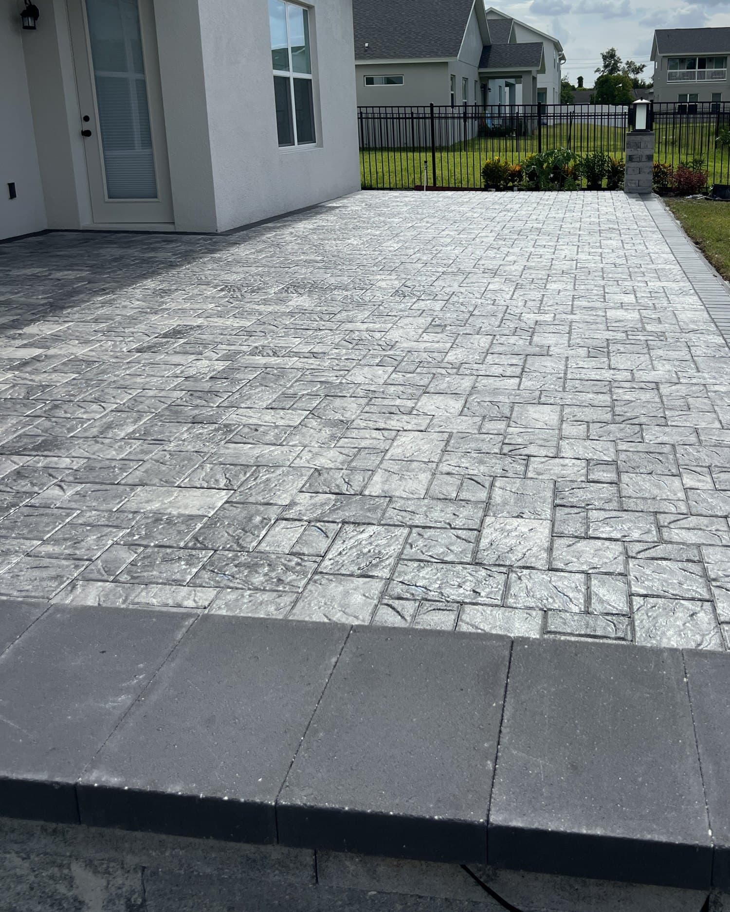 Sealed grey slate-texture paver patio with a charcoal border behind a house
