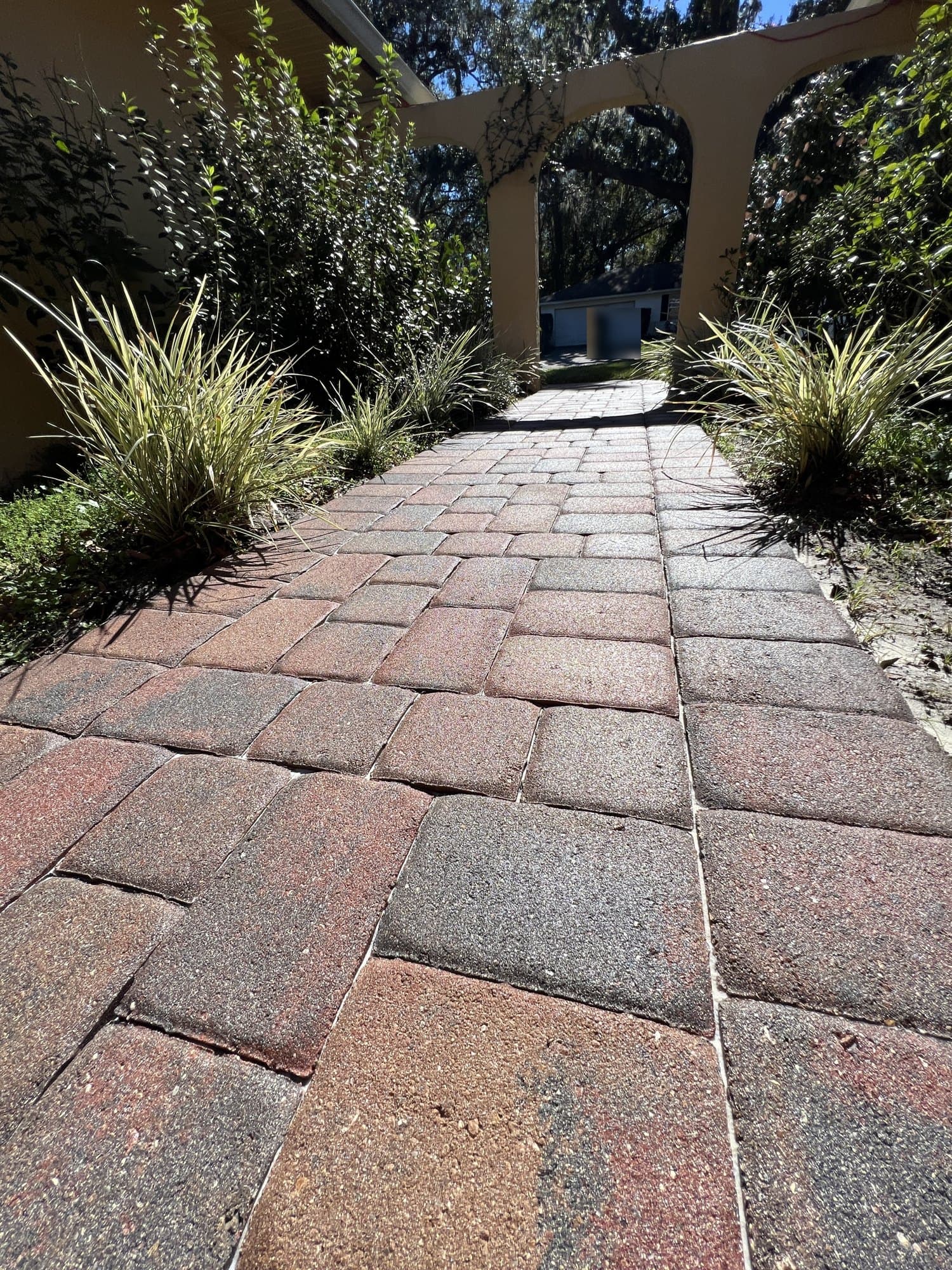 Sealed red and charcoal paver walkway running between planting beds toward stucco arches