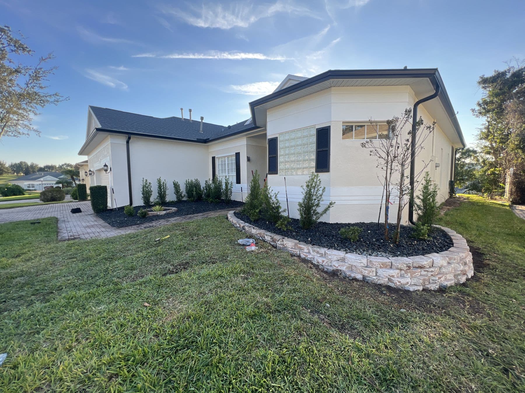 Front elevation after planting: clipped hedges along the house, black landscape rock and a curved stacked-stone garden wall
