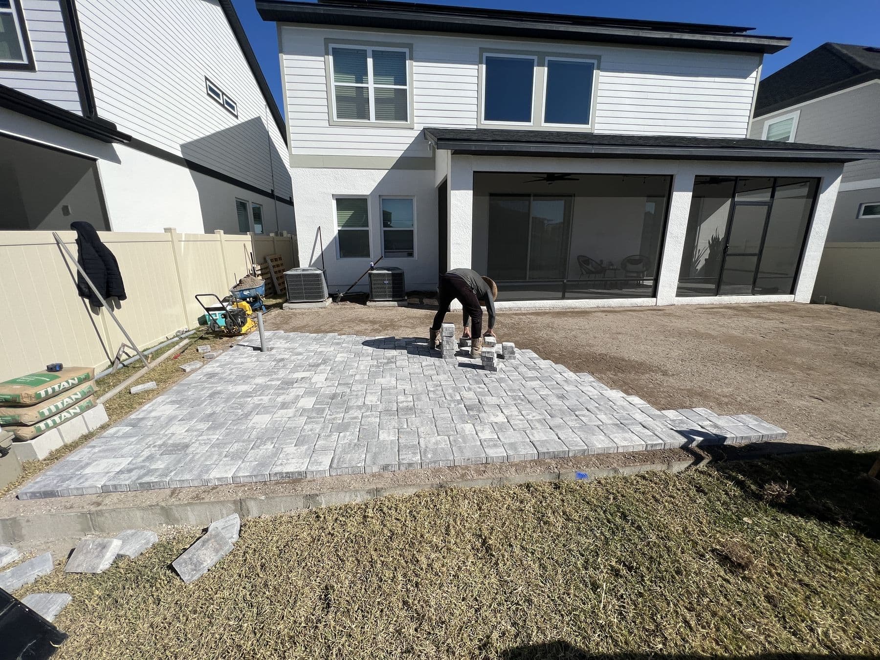 Grey pavers being laid over a compacted base, roughly half the patio complete, plate compactor and sand to one side