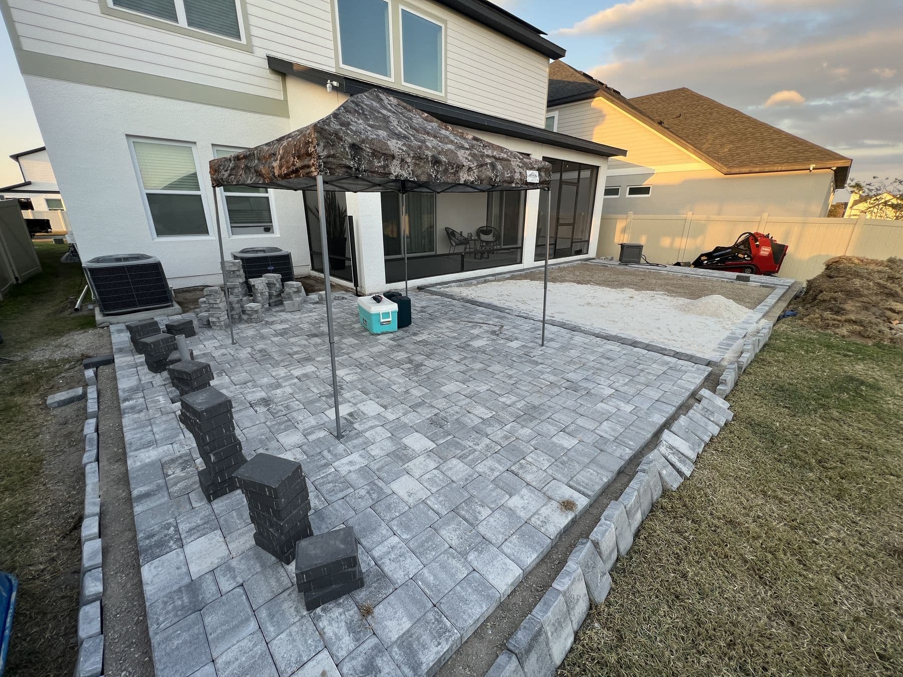 Paver field largely complete at sunset, stacks of dark grey border pavers waiting on the patio