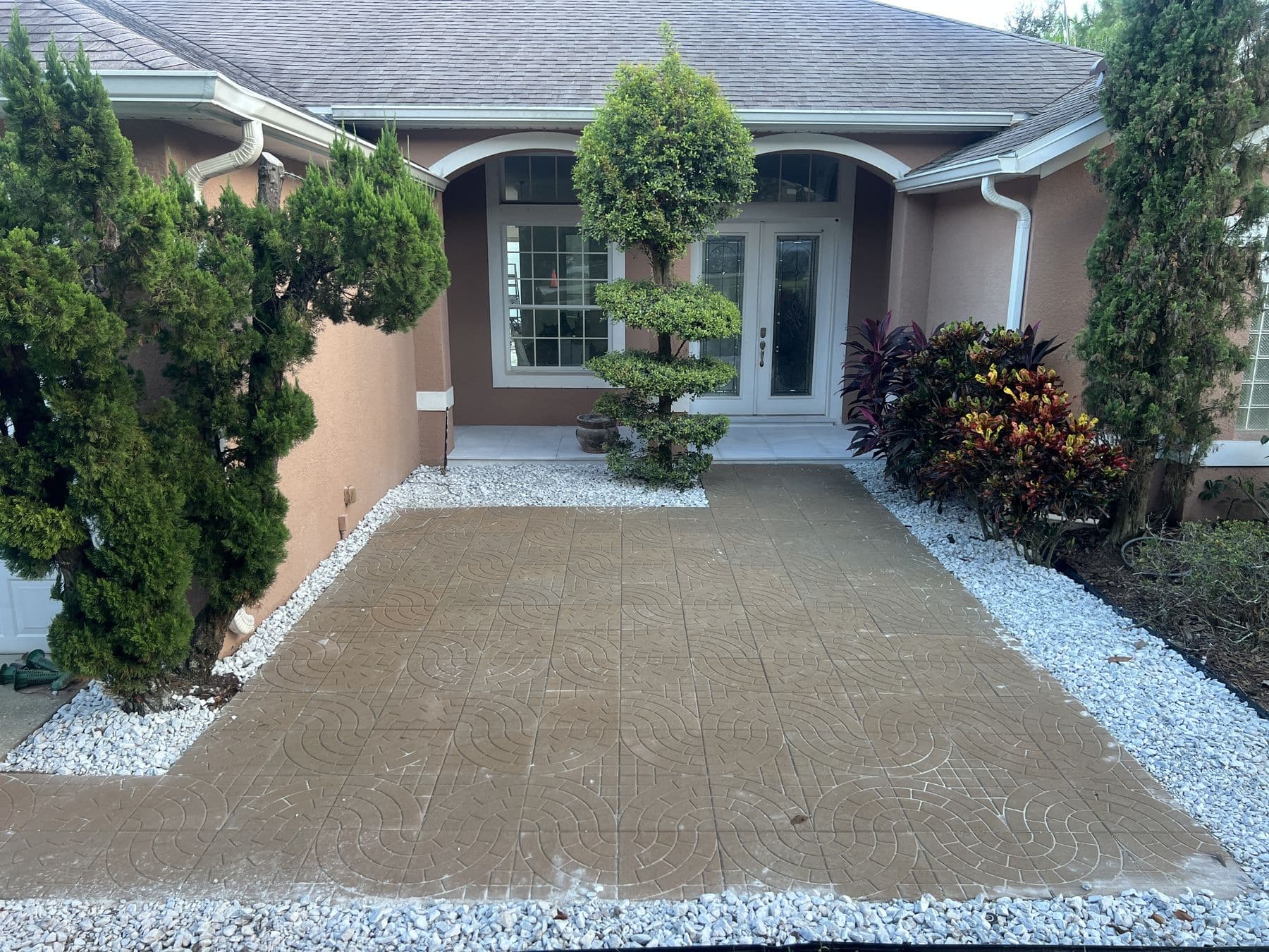 Completed front courtyard with patterned paver field, white landscape rock borders and clipped topiary