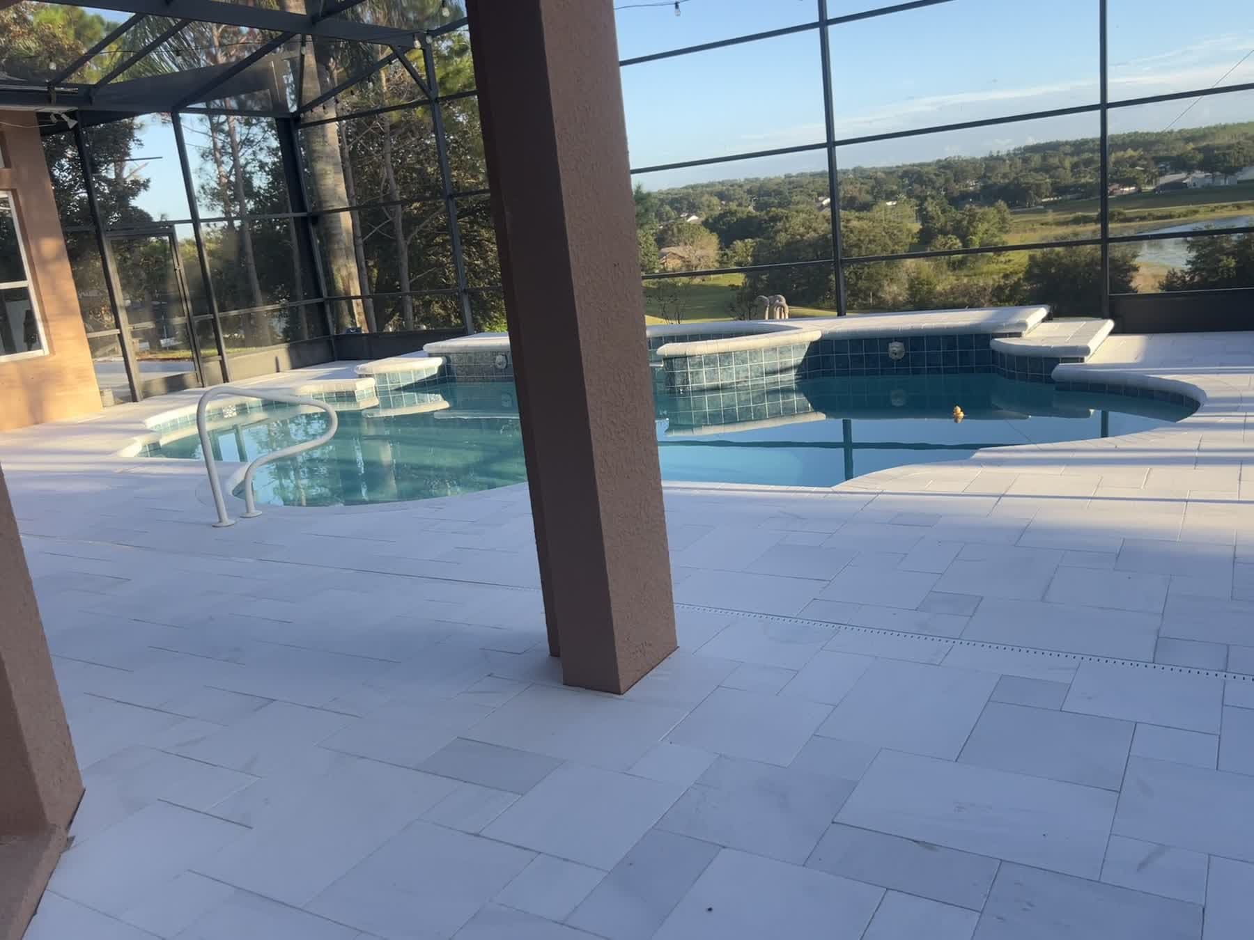 Finished travertine pool deck inside a screen enclosure, looking out across the pool to the lake beyond