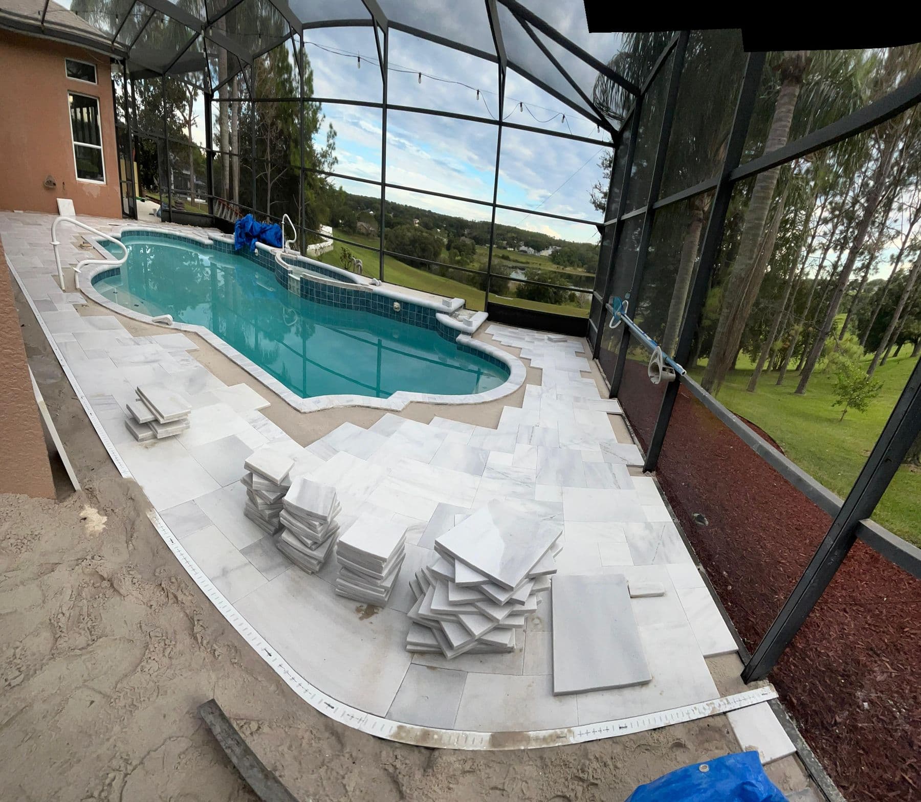 Second angle of the pool deck mid-installation, stacks of travertine tile waiting on the laid surface