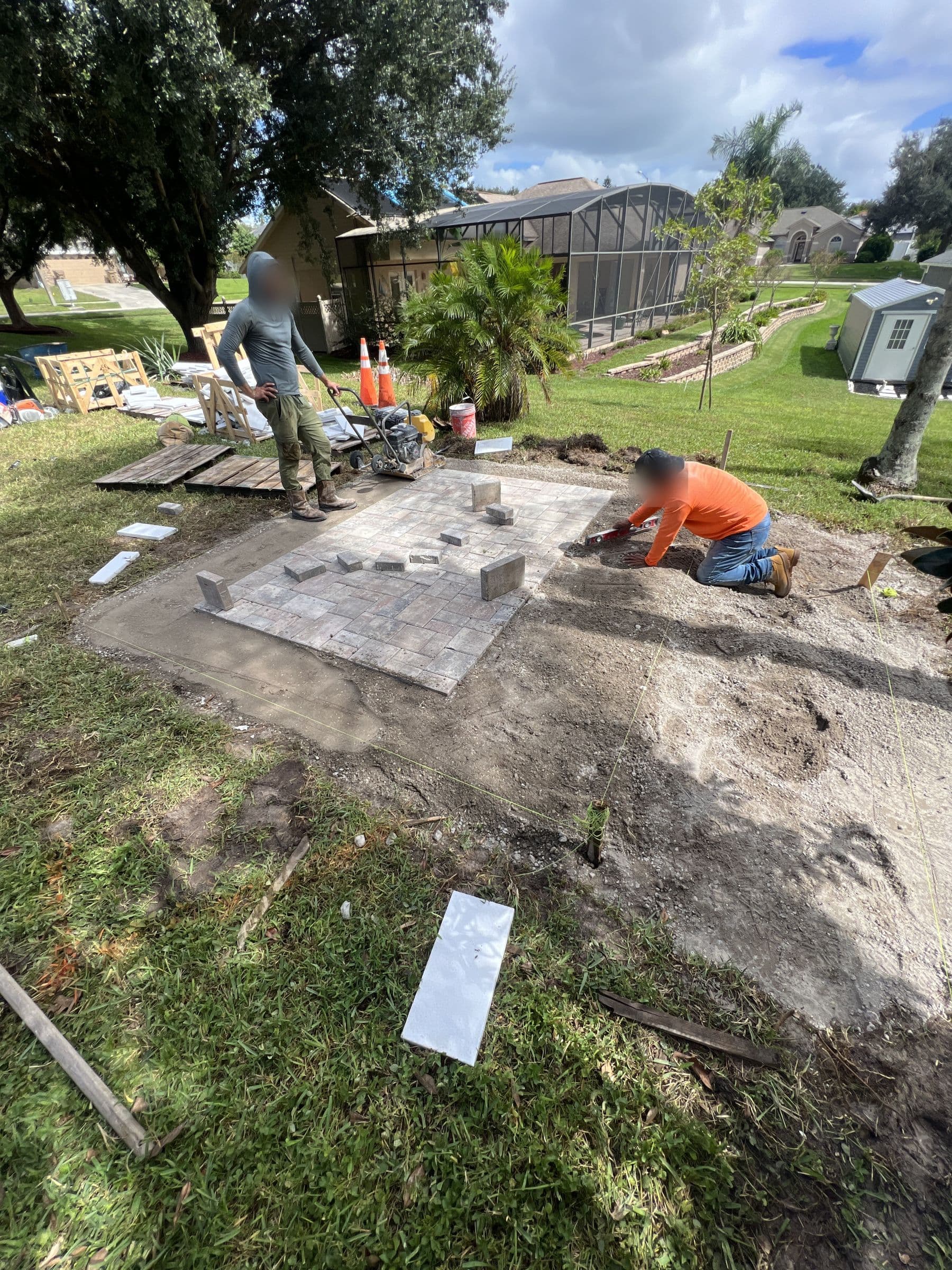 Crew setting pavers for the sauna slab on a graded slope, lake and screen enclosure behind