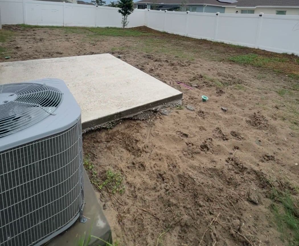 Back yard before work: bare sand and patchy grass, a small concrete slab beside the air-conditioning condenser