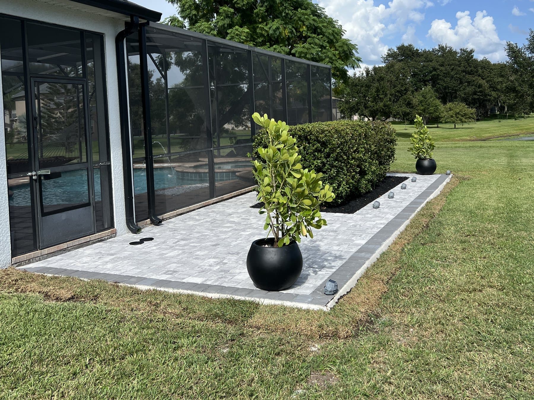 The patio from the lawn: black planters at each end, the hedge in its rock bed and the enclosure and pool behind