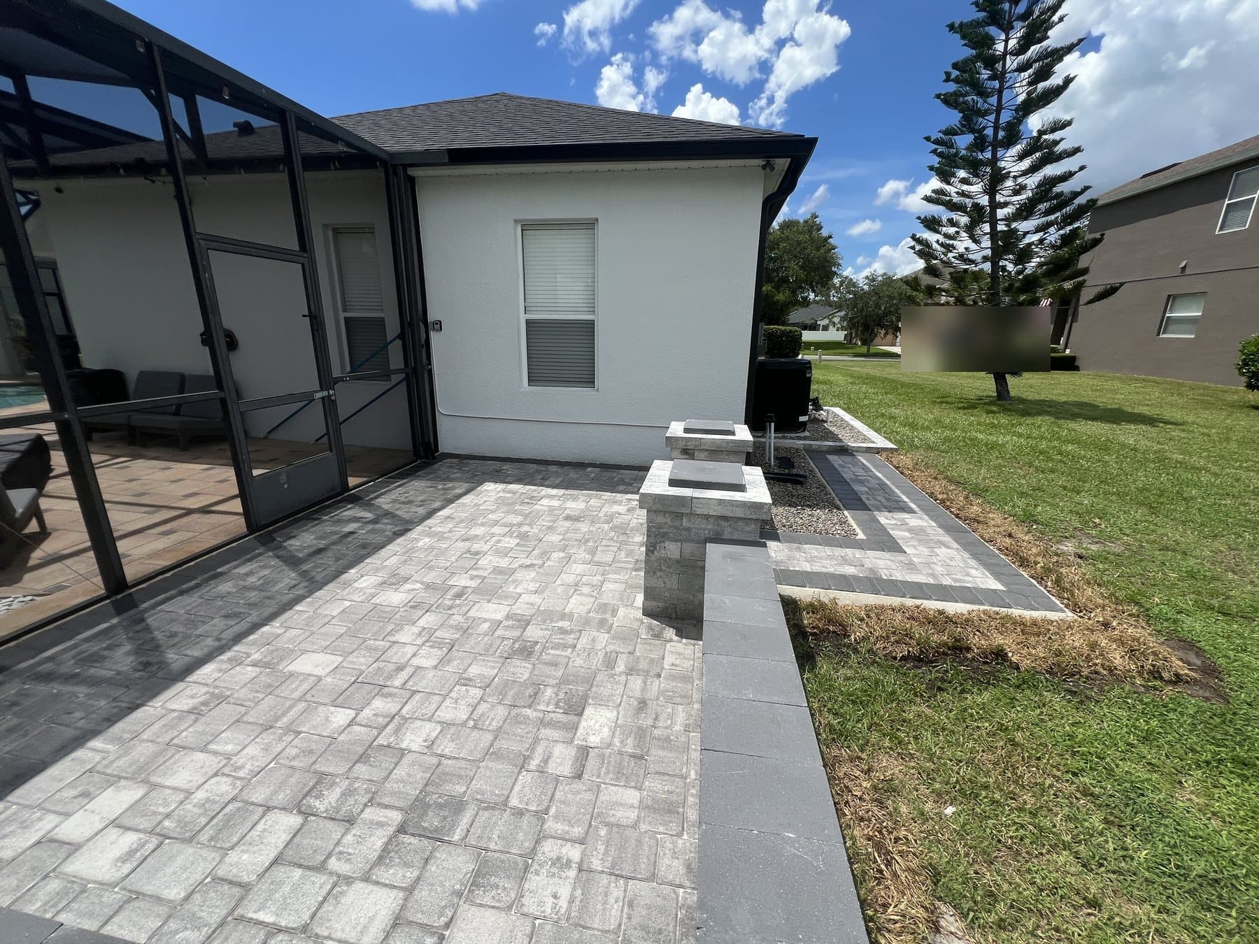 Block seat wall with two capped pillars at the end of the patio, the walkway continuing round the side of the house beyond