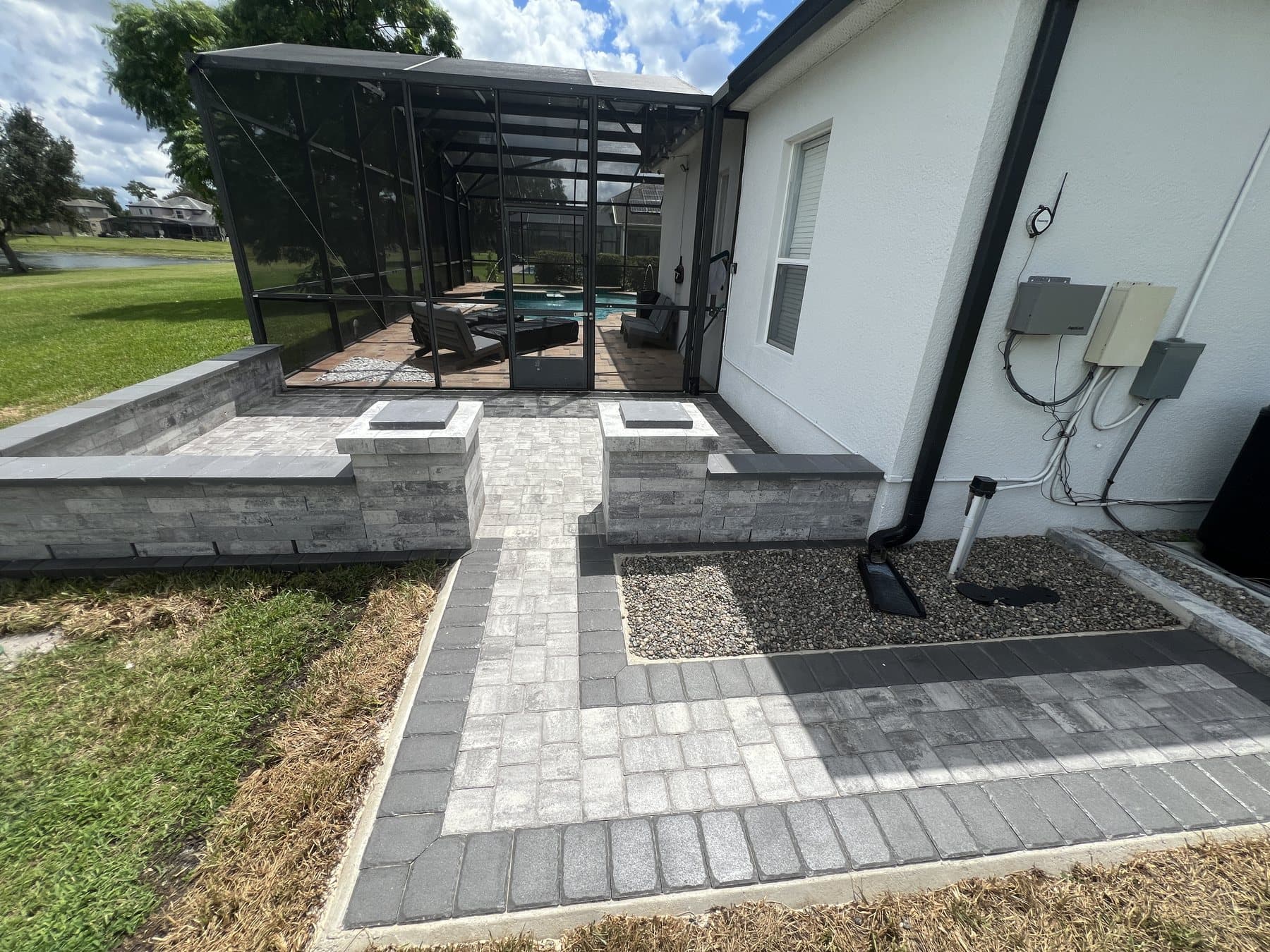 Charcoal-bordered paver walkway between capped pillars, leading to a pool enclosure