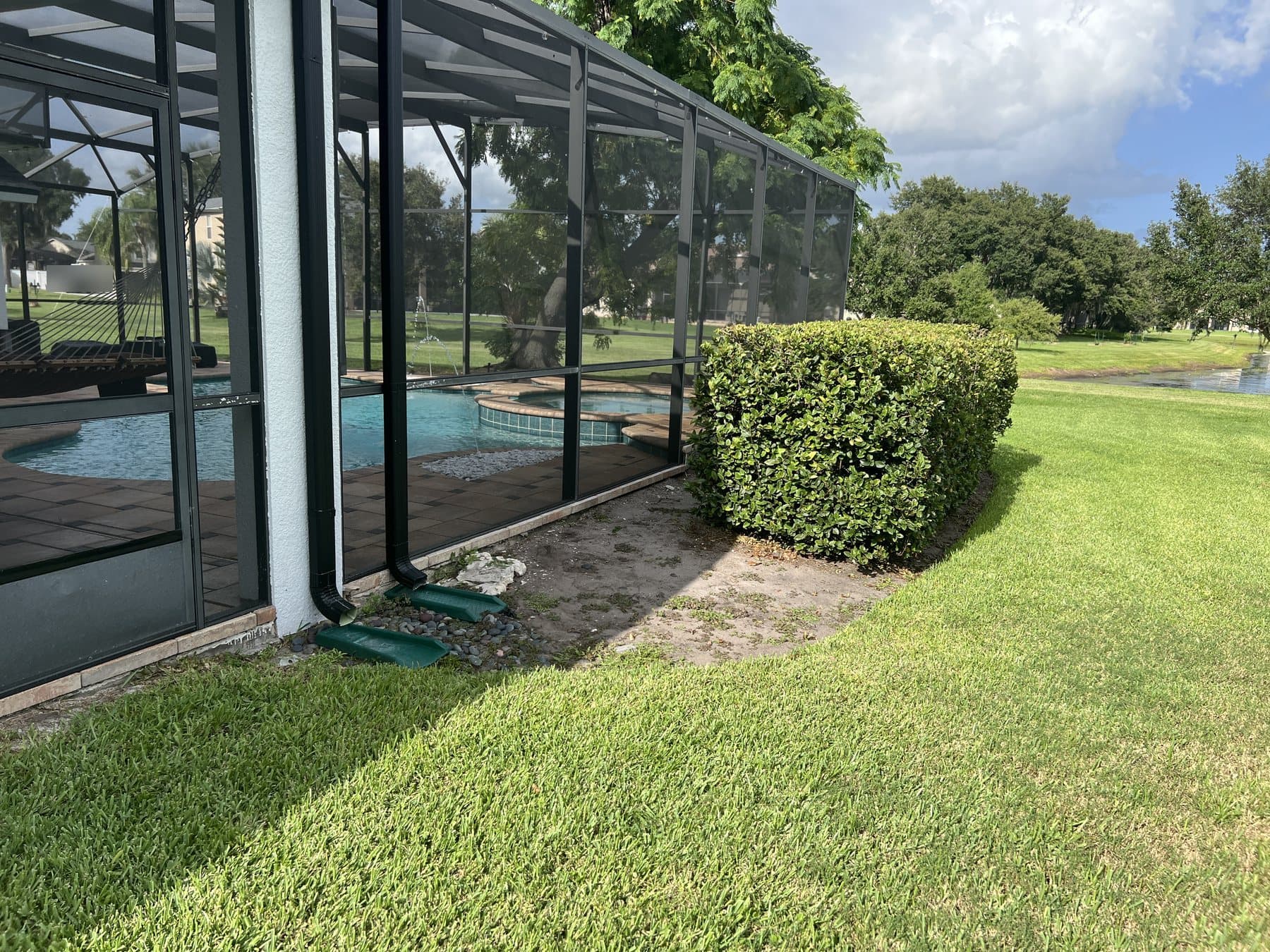 Before work: a bare strip of dirt between the enclosure and the lawn, two downspouts ending in green splash blocks, the existing hedge beyond